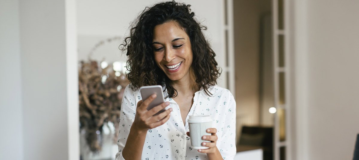 Businesswoman in office using smart phone, holding cup of coffee