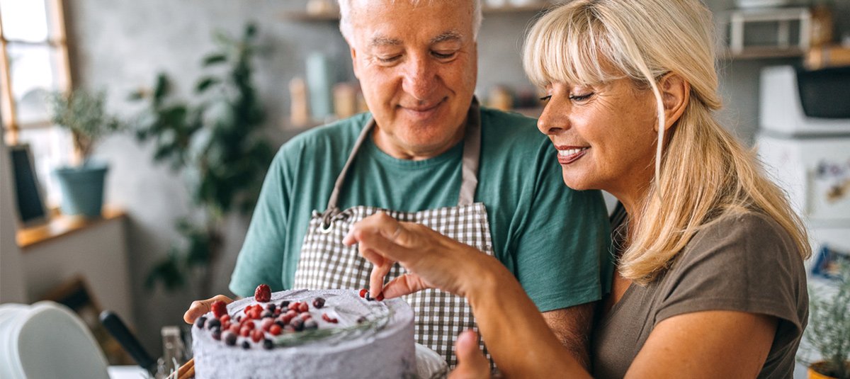 Old couple decorating cake in kitchen